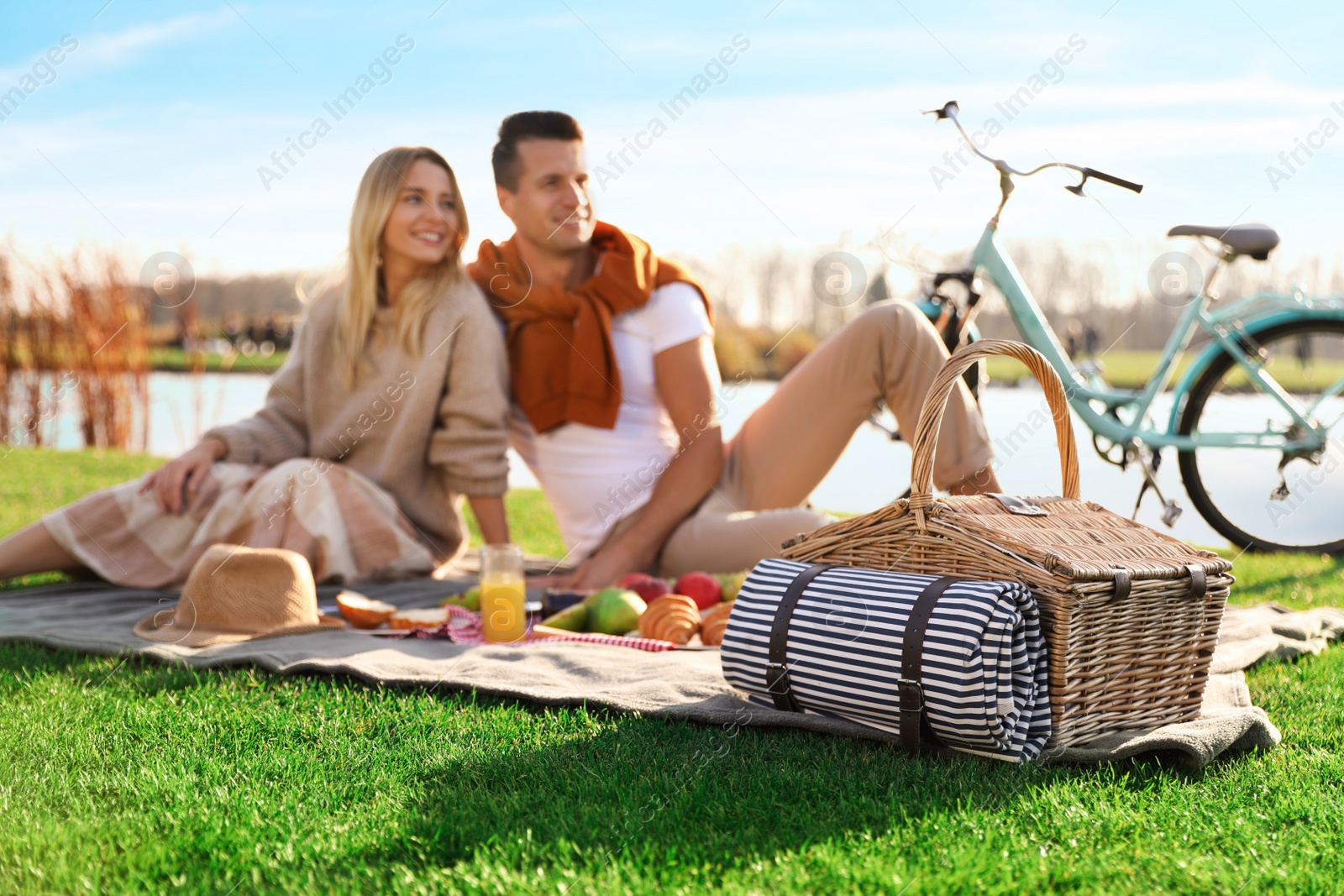 Photo of Happy young couple having picnic outdoors, focus on wicker basket
