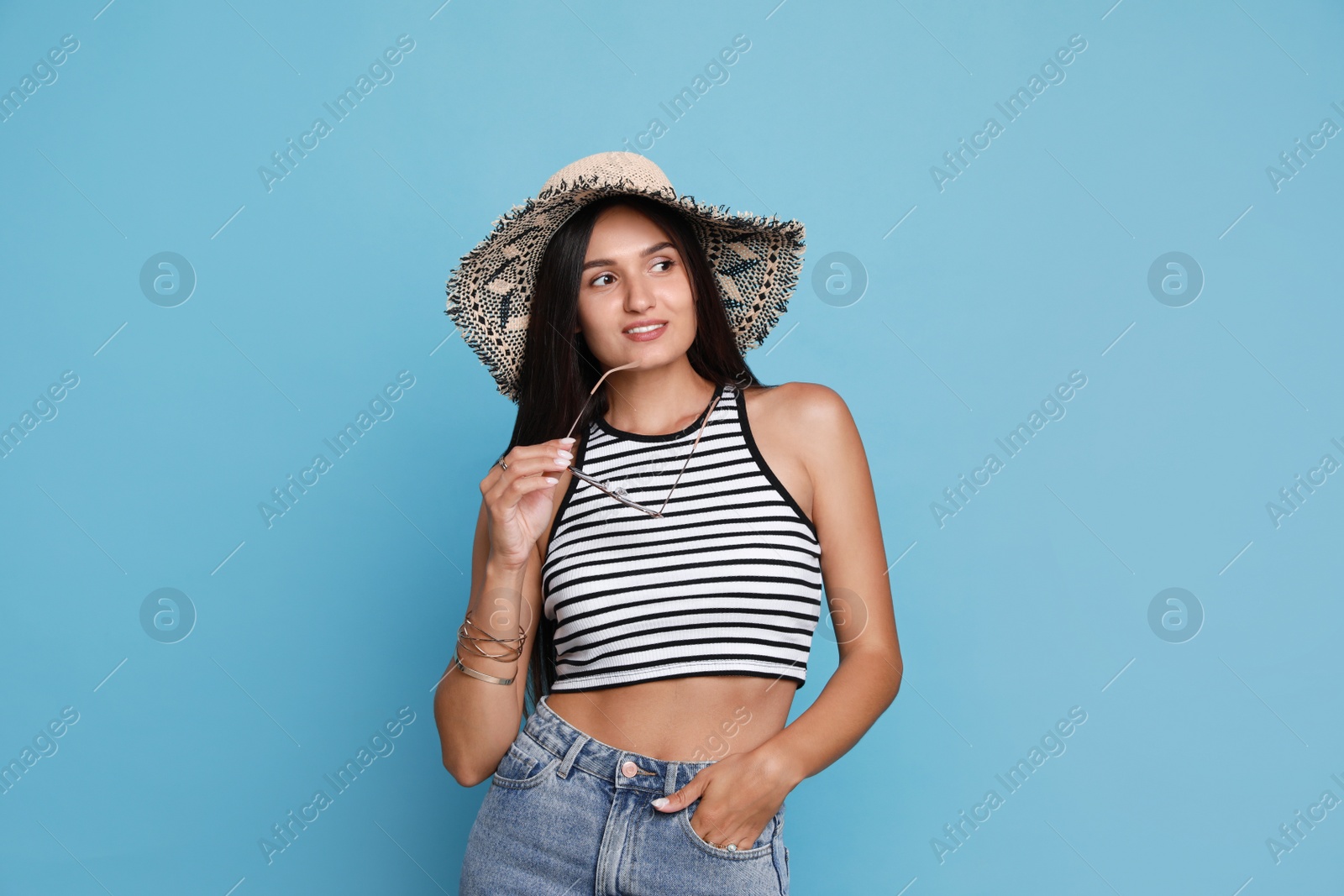 Beautiful young woman with straw hat and stylish sunglasses on light blue background Photo of Beautiful young woman with straw hat and stylish sunglasses on light blue background