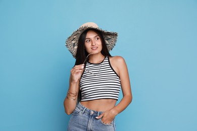 Beautiful young woman with straw hat and stylish sunglasses on light blue background Photo of Beautiful young woman with straw hat and stylish sunglasses on light blue background