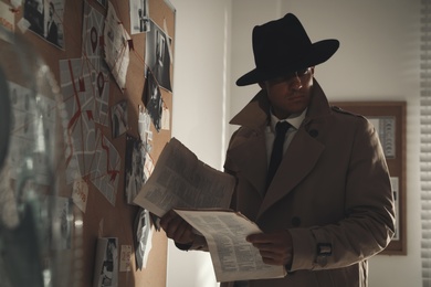 Detective with newspaper near evidence board in office Photo of Detective with newspaper near evidence board in office