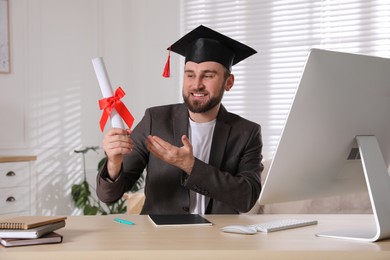 Happy student with graduation hat and diploma at workplace in office Photo of Happy student with graduation hat and diploma at workplace in office