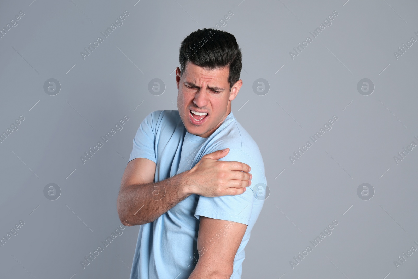 Man suffering from shoulder pain on grey background Photo of Man suffering from shoulder pain on grey background