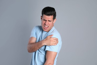 Man suffering from shoulder pain on grey background Photo of Man suffering from shoulder pain on grey background