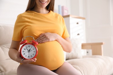 Young pregnant woman holding alarm clock near her belly at home, closeup. Time to give birth Photo of Young pregnant woman holding alarm clock near her belly at home, closeup. Time to give birth