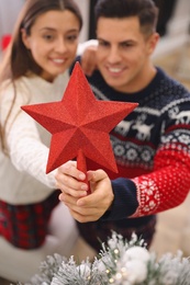 Couple decorating Christmas tree indoors, focus on star topper Photo of Couple decorating Christmas tree indoors, focus on star topper