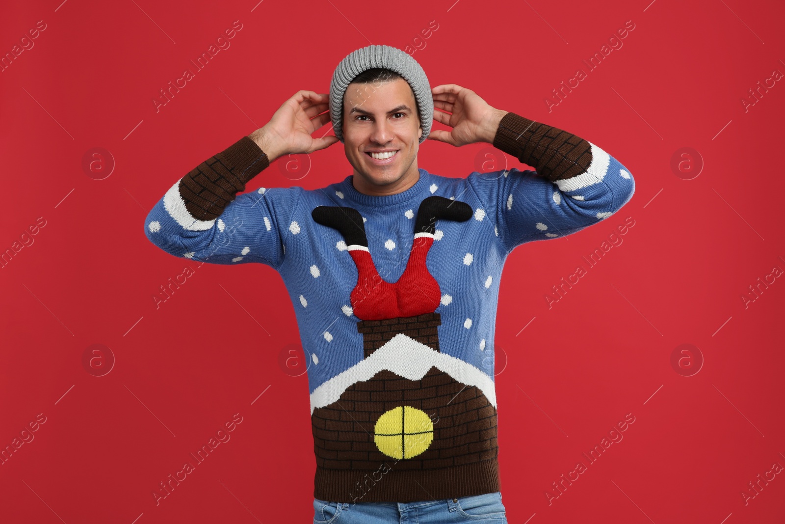 Happy man in Christmas sweater and hat on red background Photo of Happy man in Christmas sweater and hat on red background