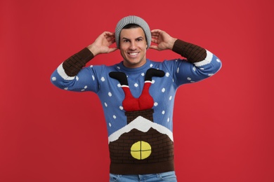 Happy man in Christmas sweater and hat on red background Photo of Happy man in Christmas sweater and hat on red background