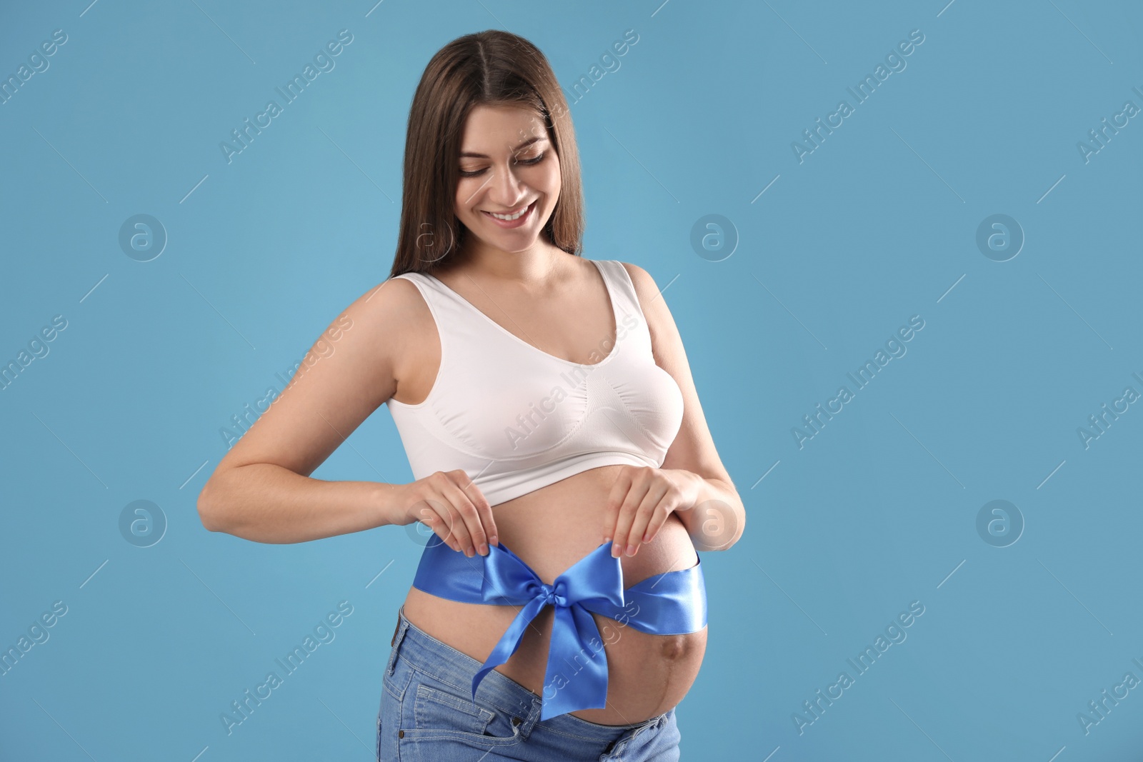 Young pregnant woman with bow on her belly against light blue background. Time to give birth Photo of Young pregnant woman with bow on her belly against light blue background. Time to give birth