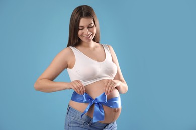 Young pregnant woman with bow on her belly against light blue background. Time to give birth Photo of Young pregnant woman with bow on her belly against light blue background. Time to give birth