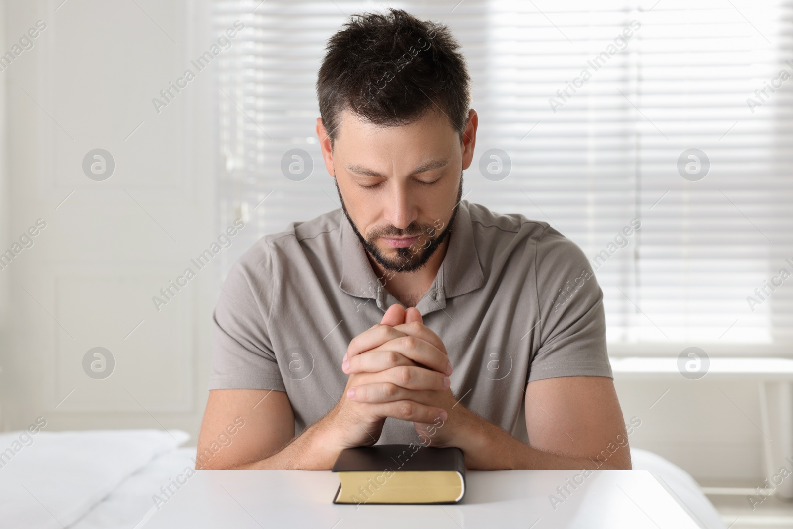 Religious man with Bible praying at home Photo of Religious man with Bible praying at home