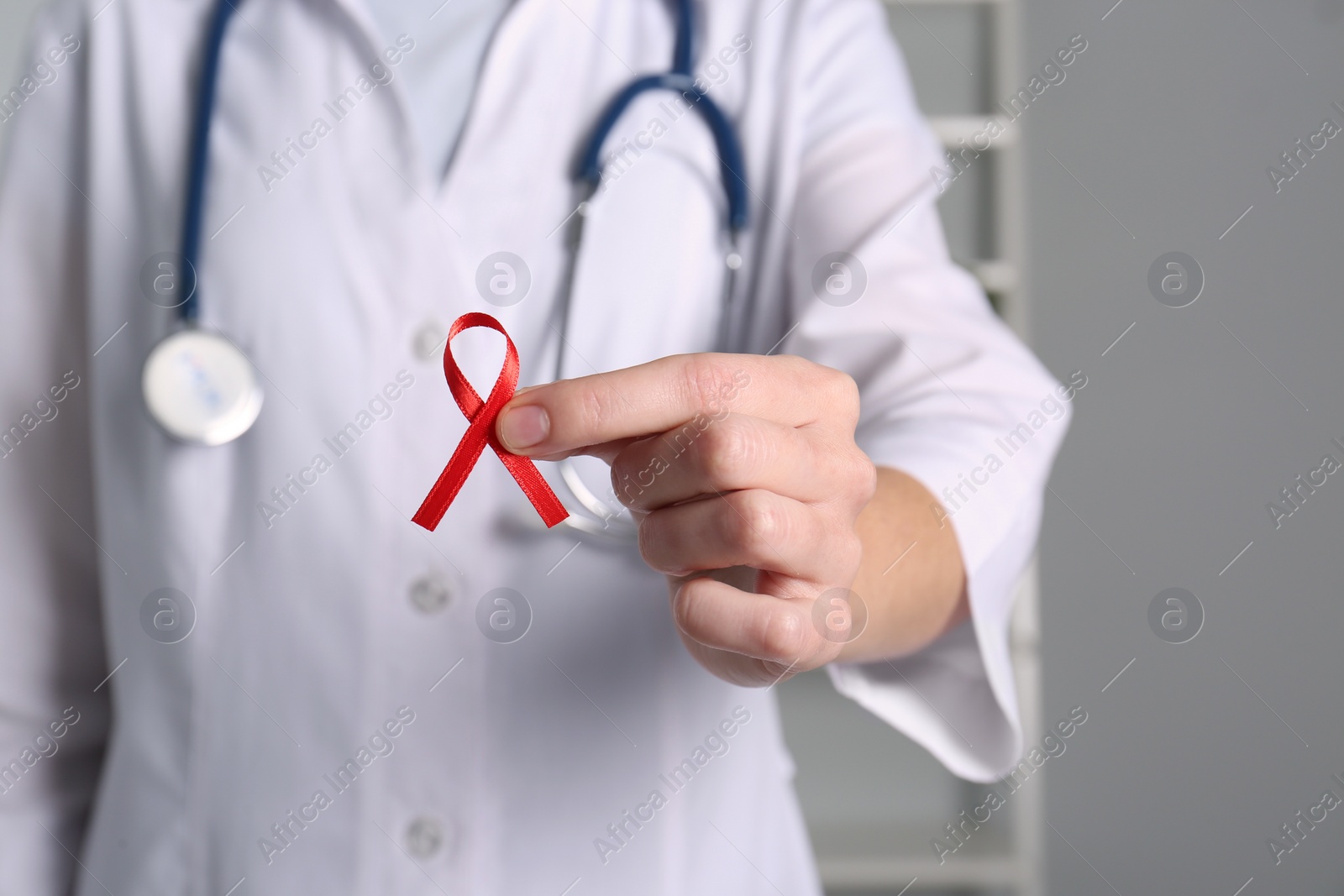 Doctor holding red awareness ribbon indoors, closeup. World AIDS disease day Photo of Doctor holding red awareness ribbon indoors, closeup. World AIDS disease day