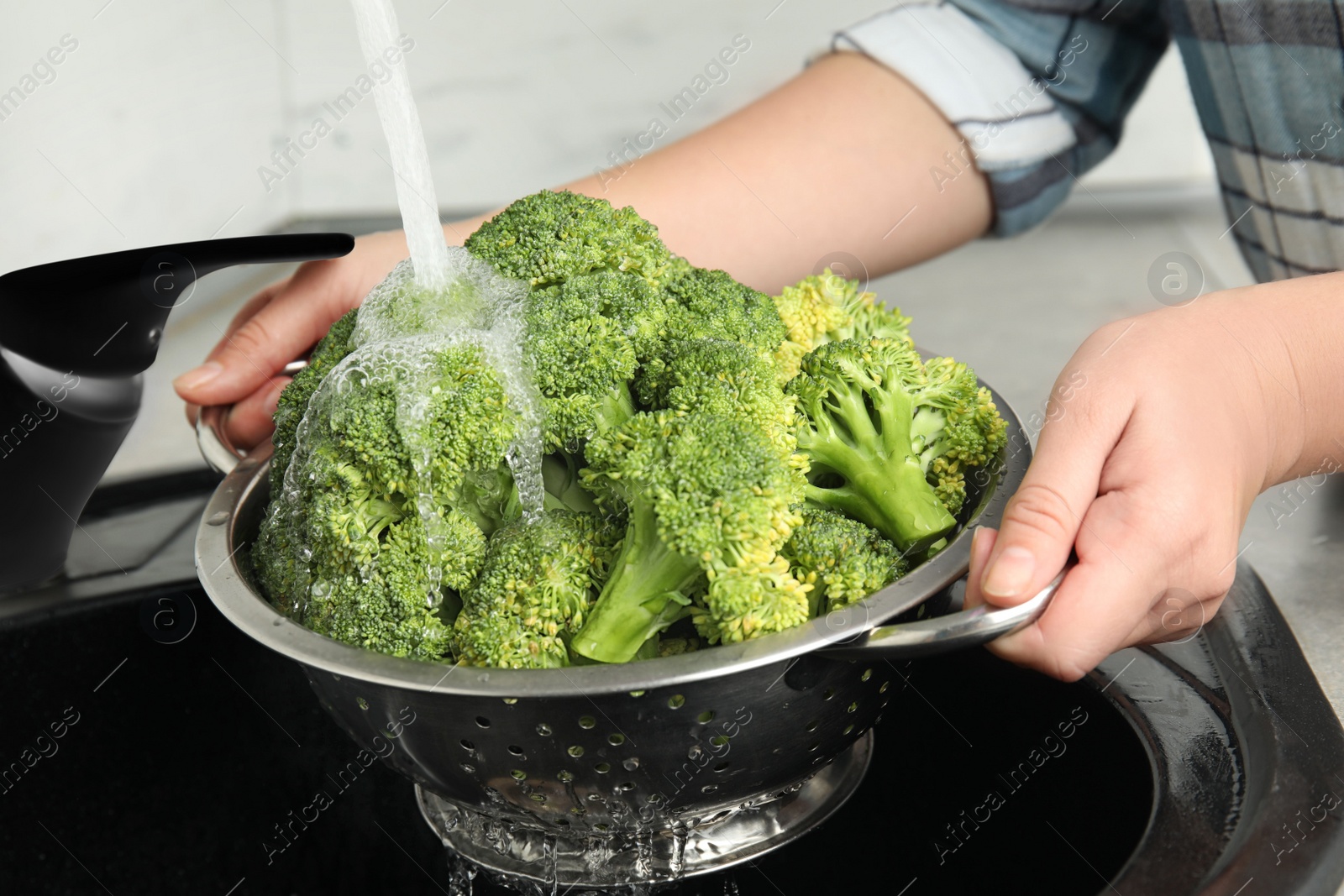 Woman washing fresh green broccoli in kitchen sink, closeup Photo of Woman washing fresh green broccoli in kitchen sink, closeup