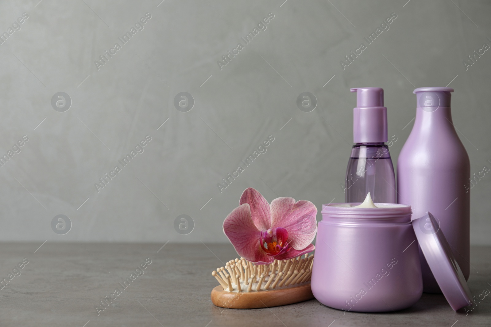 Different hair products, flower and brush on grey table. Space for text Photo of Different hair products, flower and brush on grey table. Space for text