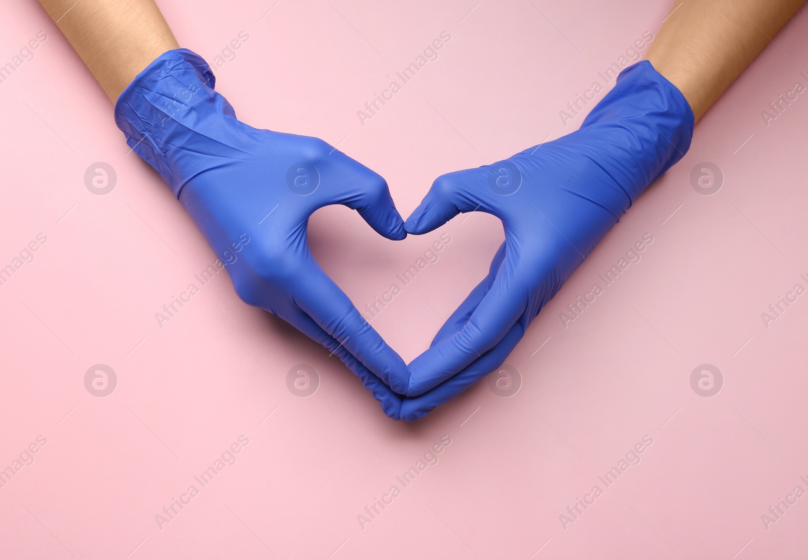 Person in medical gloves showing heart gesture against pink background, closeup of hands Photo of Person in medical gloves showing heart gesture against pink background, closeup of hands