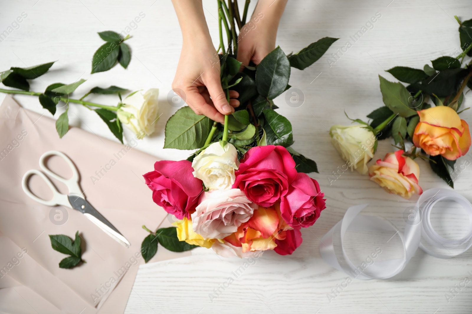 Woman making luxury bouquet of fresh roses at white wooden table, top view Photo of Woman making luxury bouquet of fresh roses at white wooden table, top view