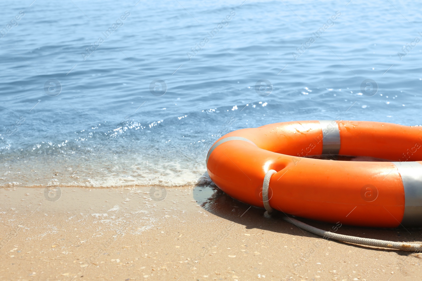 Orange life buoy on sand near sea, closeup. Emergency rescue equipment Photo of Orange life buoy on sand near sea, closeup. Emergency rescue equipment