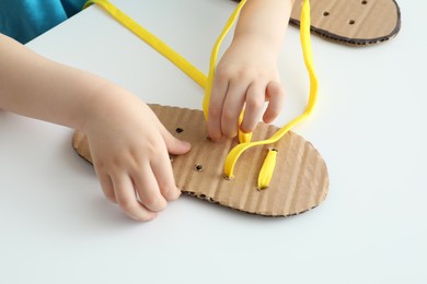 Little boy tying shoe lace using training cardboard template at white table, closeup Photo of Little boy tying shoe lace using training cardboard template at white table, closeup