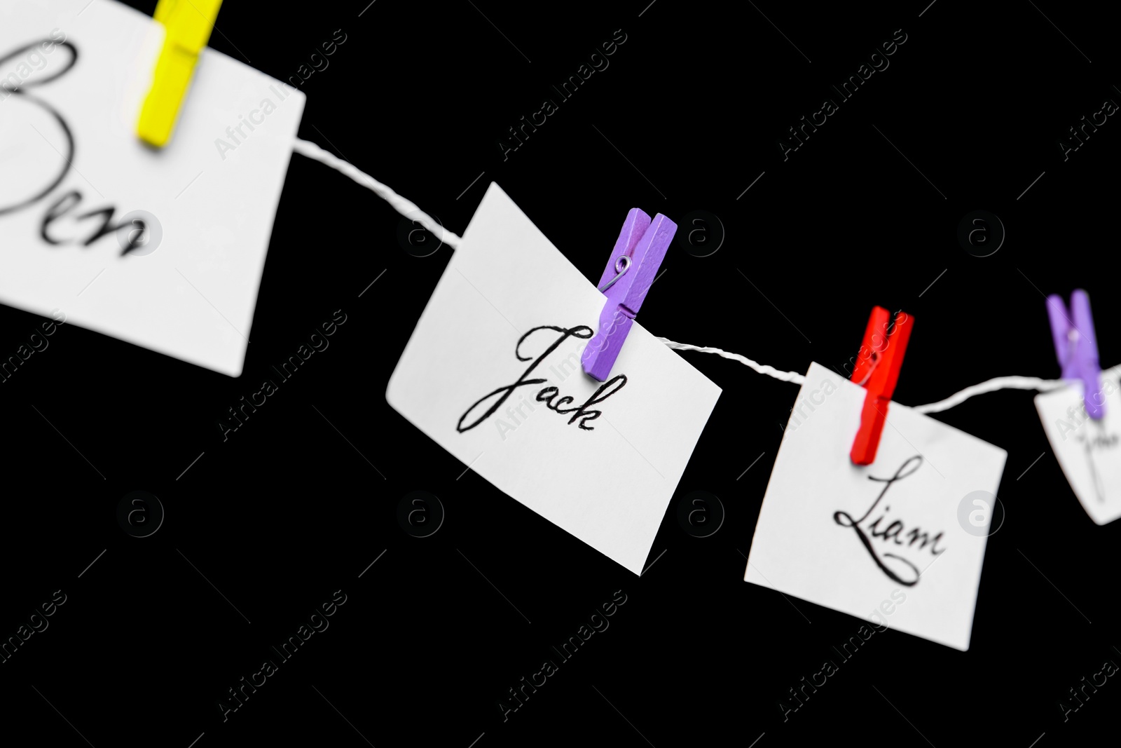 Paper pieces with baby names on rope against black background, closeup Photo of Paper pieces with baby names on rope against black background, closeup