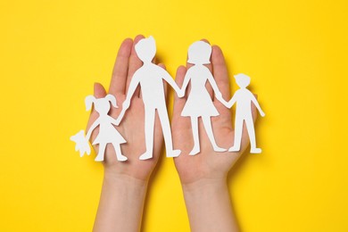 Woman holding paper family figures on yellow background, top view Photo of Woman holding paper family figures on yellow background, top view