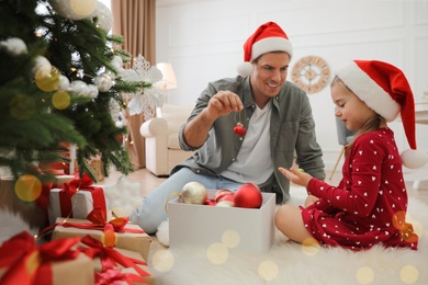 Father with his cute daughter in Santa hats decorating Christmas tree together at home Photo of Father with his cute daughter in Santa hats decorating Christmas tree together at home