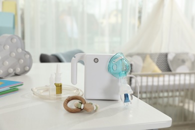 Modern nebulizer, medicines and wooden baby toy on white table in children's room. Equipment for inhalation Photo of Modern nebulizer, medicines and wooden baby toy on white table in children's room. Equipment for inhalation