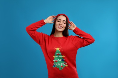 Young woman in Christmas sweater and hat on blue background Photo of Young woman in Christmas sweater and hat on blue background