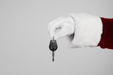 Santa Claus holding car key on light grey background, closeup of hand Photo of Santa Claus holding car key on light grey background, closeup of hand