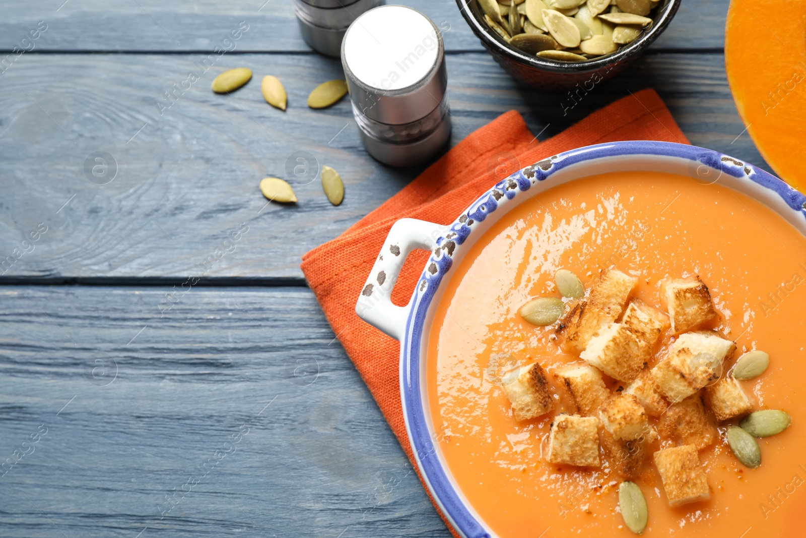 Tasty creamy pumpkin soup with croutons and seeds in bowl on blue wooden table, flat lay. Space for text Photo of Tasty creamy pumpkin soup with croutons and seeds in bowl on blue wooden table, flat lay. Space for text
