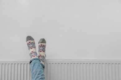 Woman warming legs on heating radiator near white wall, closeup. Space for text Photo of Woman warming legs on heating radiator near white wall, closeup. Space for text