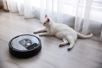 Modern robotic vacuum cleaner and cute cat on floor indoors Photo of Modern robotic vacuum cleaner and cute cat on floor indoors