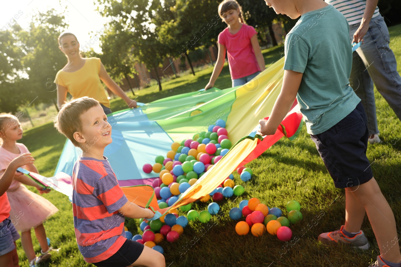 Group of children and teacher playing with rainbow playground parachute on green grass. Summer camp activity Photo of Group of children and teacher playing with rainbow playground parachute on green grass. Summer camp activity