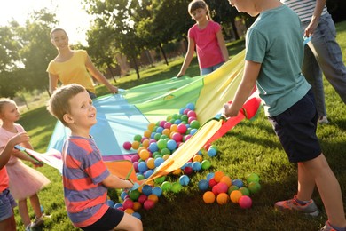Group of children and teacher playing with rainbow playground parachute on green grass. Summer camp activity Photo of Group of children and teacher playing with rainbow playground parachute on green grass. Summer camp activity