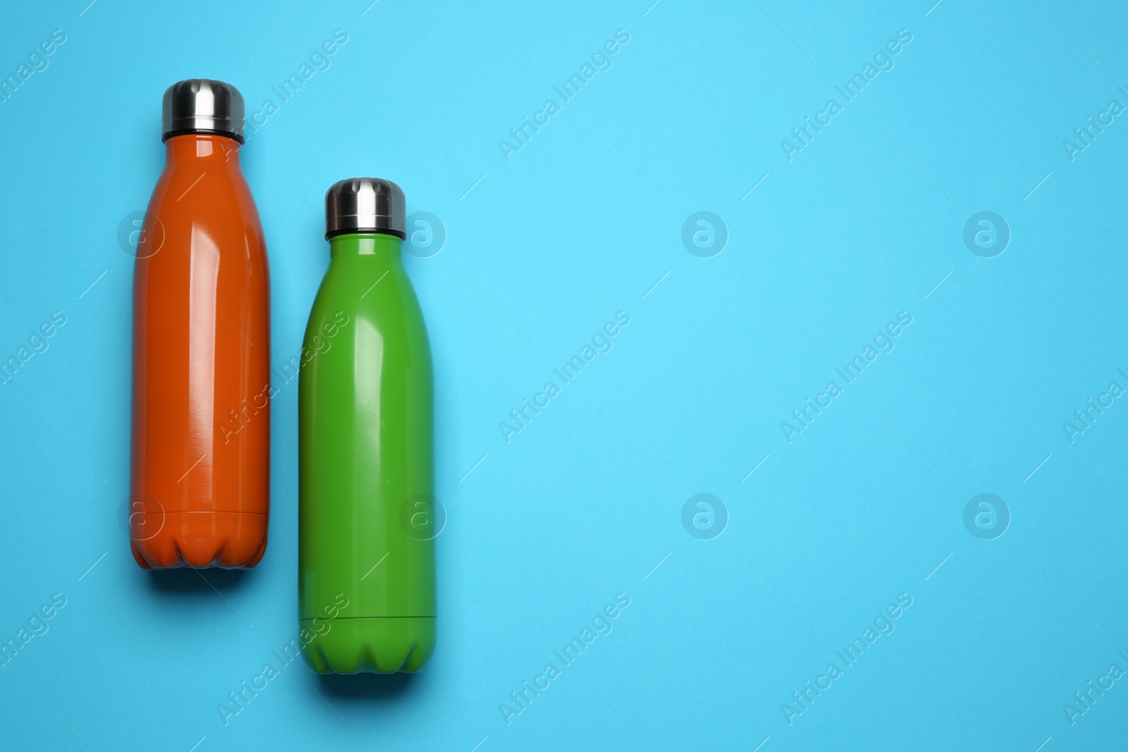Modern thermo bottles on light blue background, flat lay. Space for text Photo of Modern thermo bottles on light blue background, flat lay. Space for text