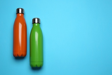 Modern thermo bottles on light blue background, flat lay. Space for text Photo of Modern thermo bottles on light blue background, flat lay. Space for text