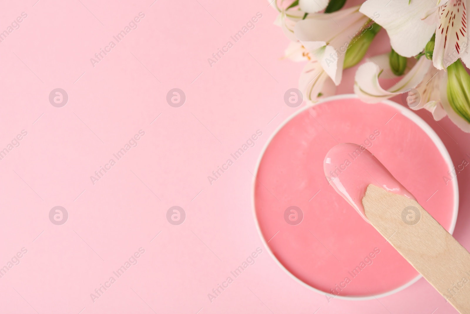 Photo of Wooden spatula, hot depilatory wax and flowers on light pink background, flat lay. Space for text