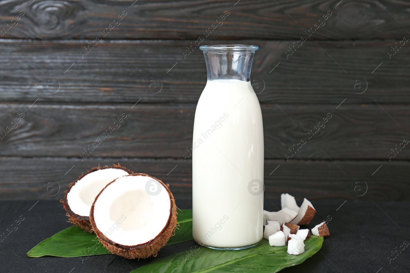 Bottle of coconut milk with fresh nuts on wooden table Photo of Bottle of coconut milk with fresh nuts on wooden table