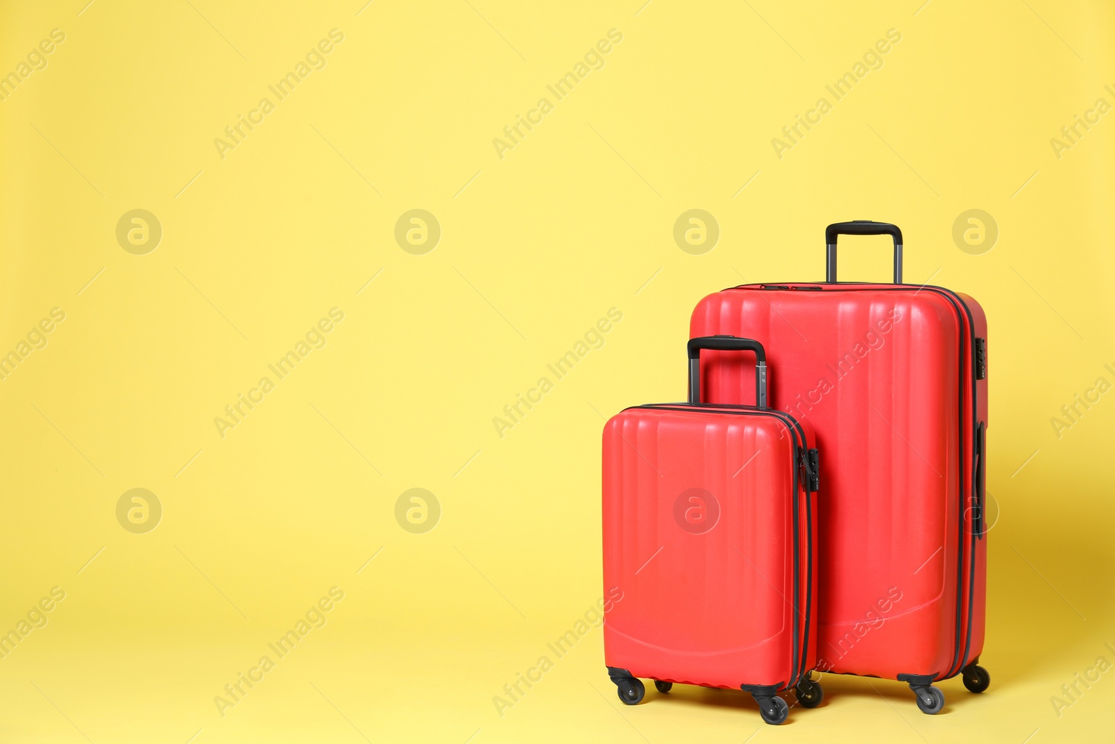 Photo of Stylish red suitcases on yellow background. Space for text