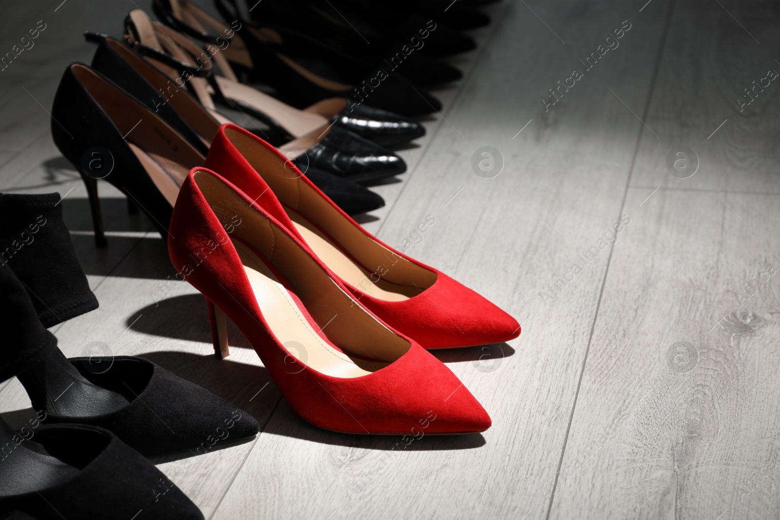 Red shoes among black ones on light wooden floor. Diversity concept Photo of Red shoes among black ones on light wooden floor. Diversity concept