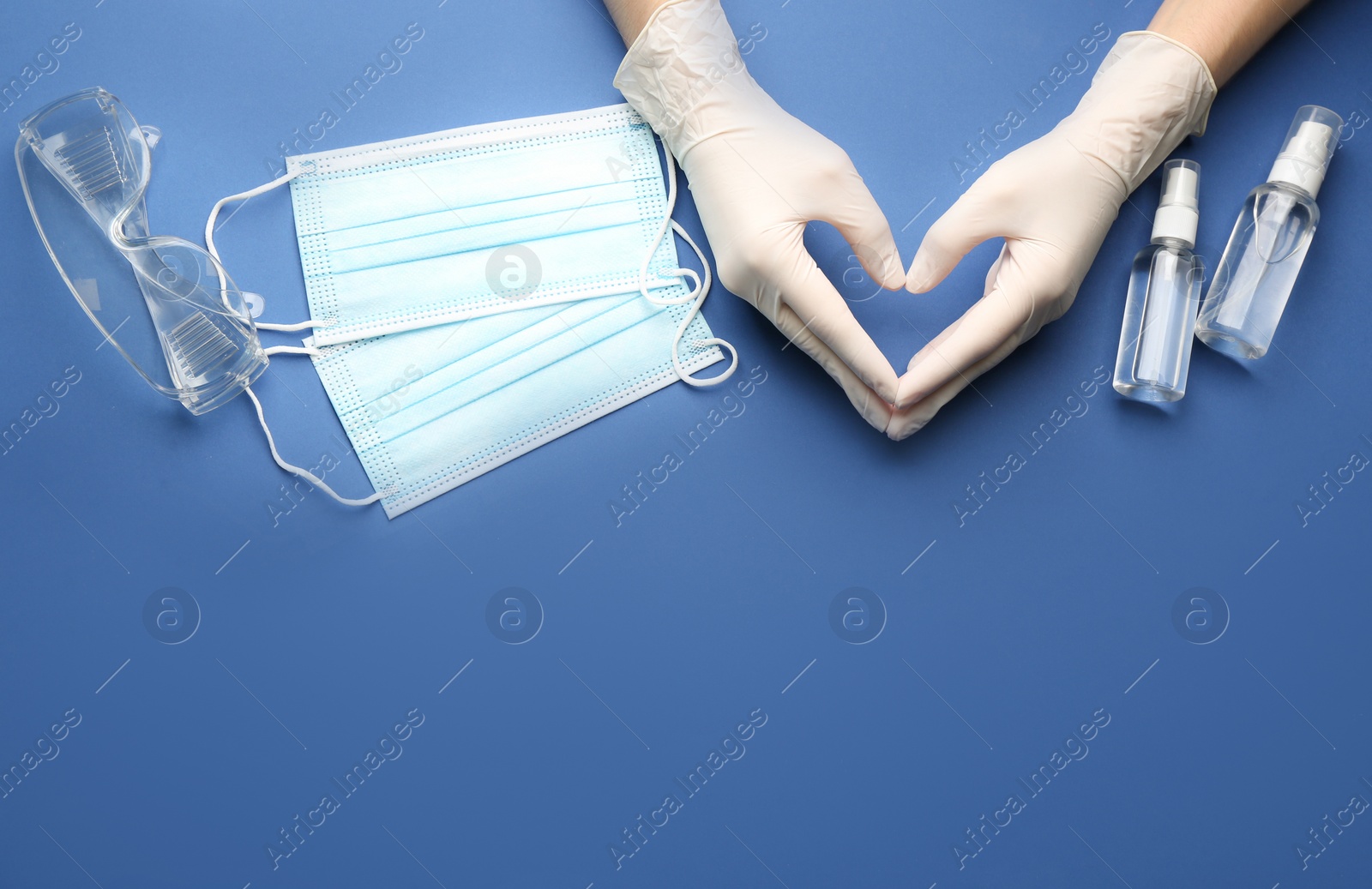 Person in gloves showing heart gesture surrounded by medical items on blue background, top view. Space for text Photo of Person in gloves showing heart gesture surrounded by medical items on blue background, top view. Space for text