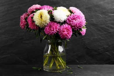 Beautiful asters in vase on table against black background. Autumn flowers Photo of Beautiful asters in vase on table against black background. Autumn flowers
