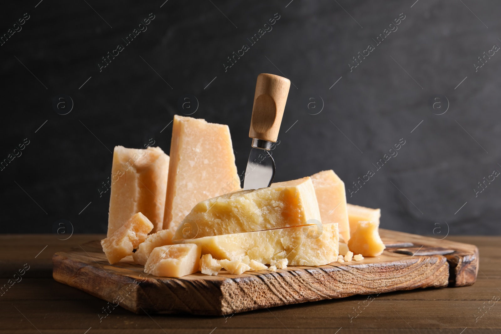 Photo of Parmesan cheese with board and knife on wooden table