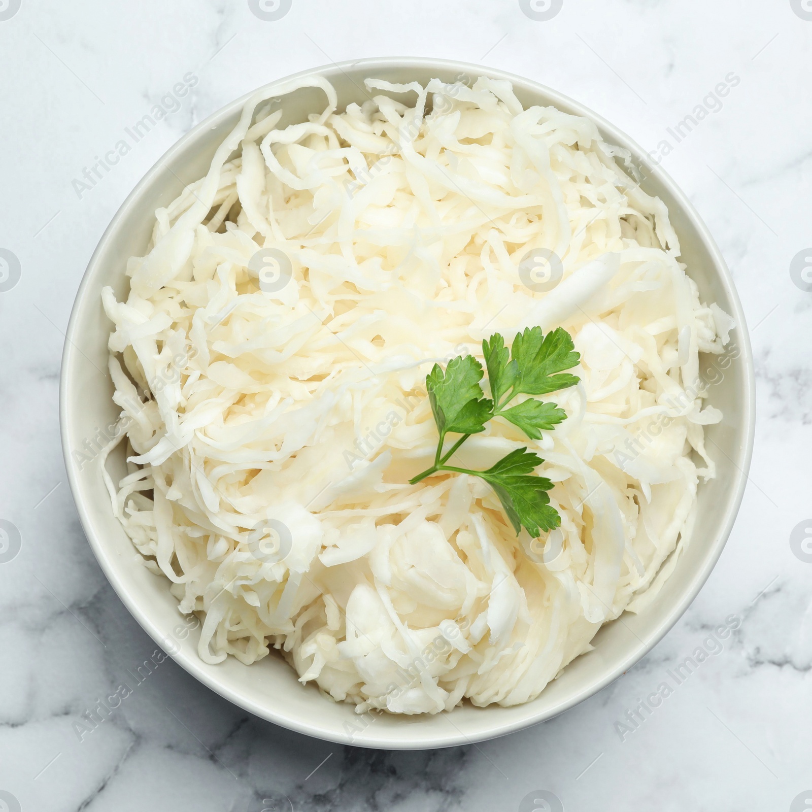 Tasty fermented cabbage with parsley on white marble table, top view Photo of Tasty fermented cabbage with parsley on white marble table, top view