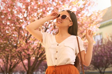 Happy stylish young woman near blossoming sakura tree outdoors. Spring look Photo of Happy stylish young woman near blossoming sakura tree outdoors. Spring look