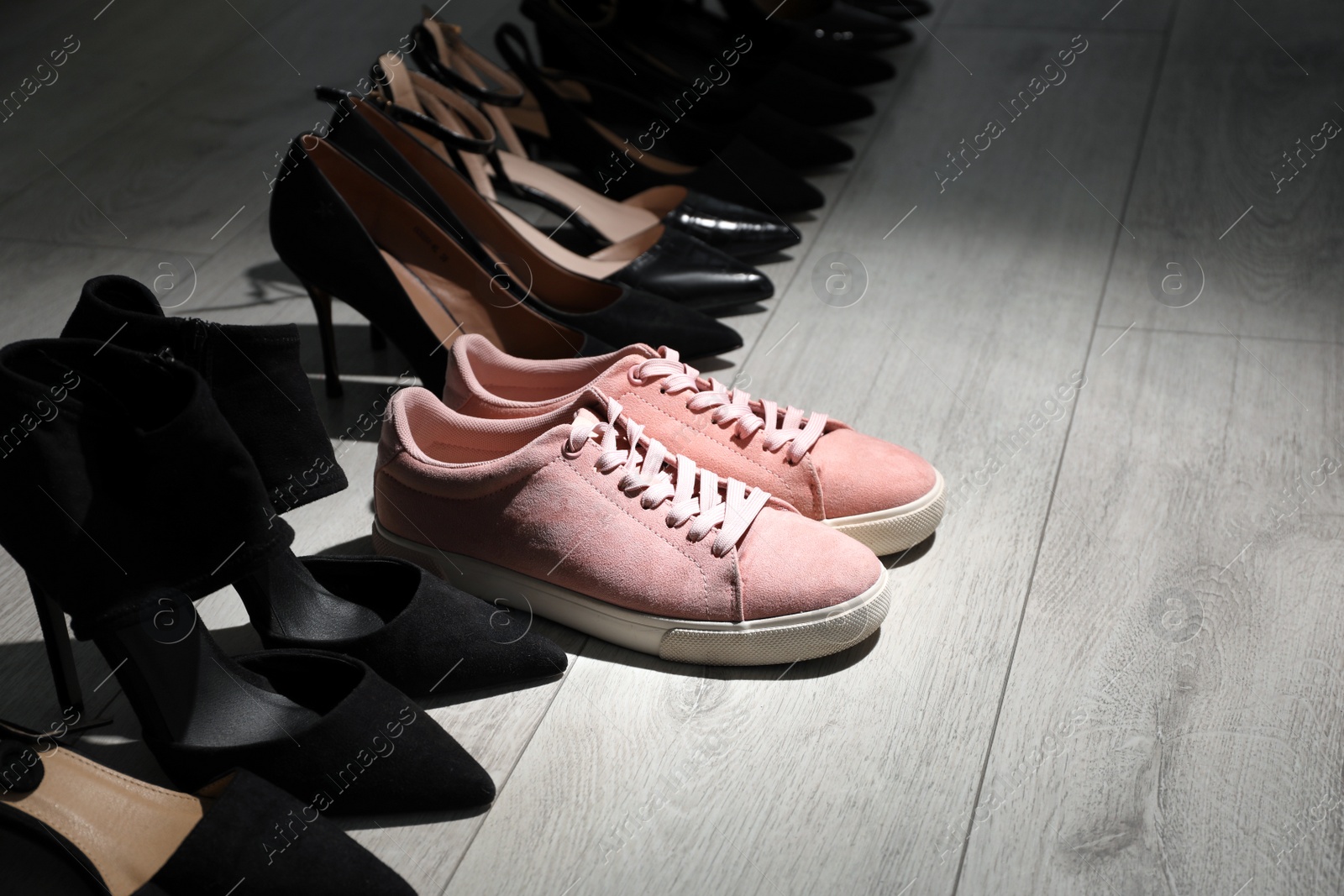 Sportive sneakers among high heeled shoes on light wooden floor. Diversity concept Photo of Sportive sneakers among high heeled shoes on light wooden floor. Diversity concept