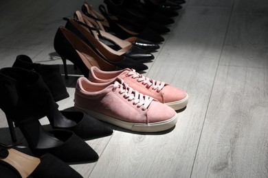 Sportive sneakers among high heeled shoes on light wooden floor. Diversity concept Photo of Sportive sneakers among high heeled shoes on light wooden floor. Diversity concept