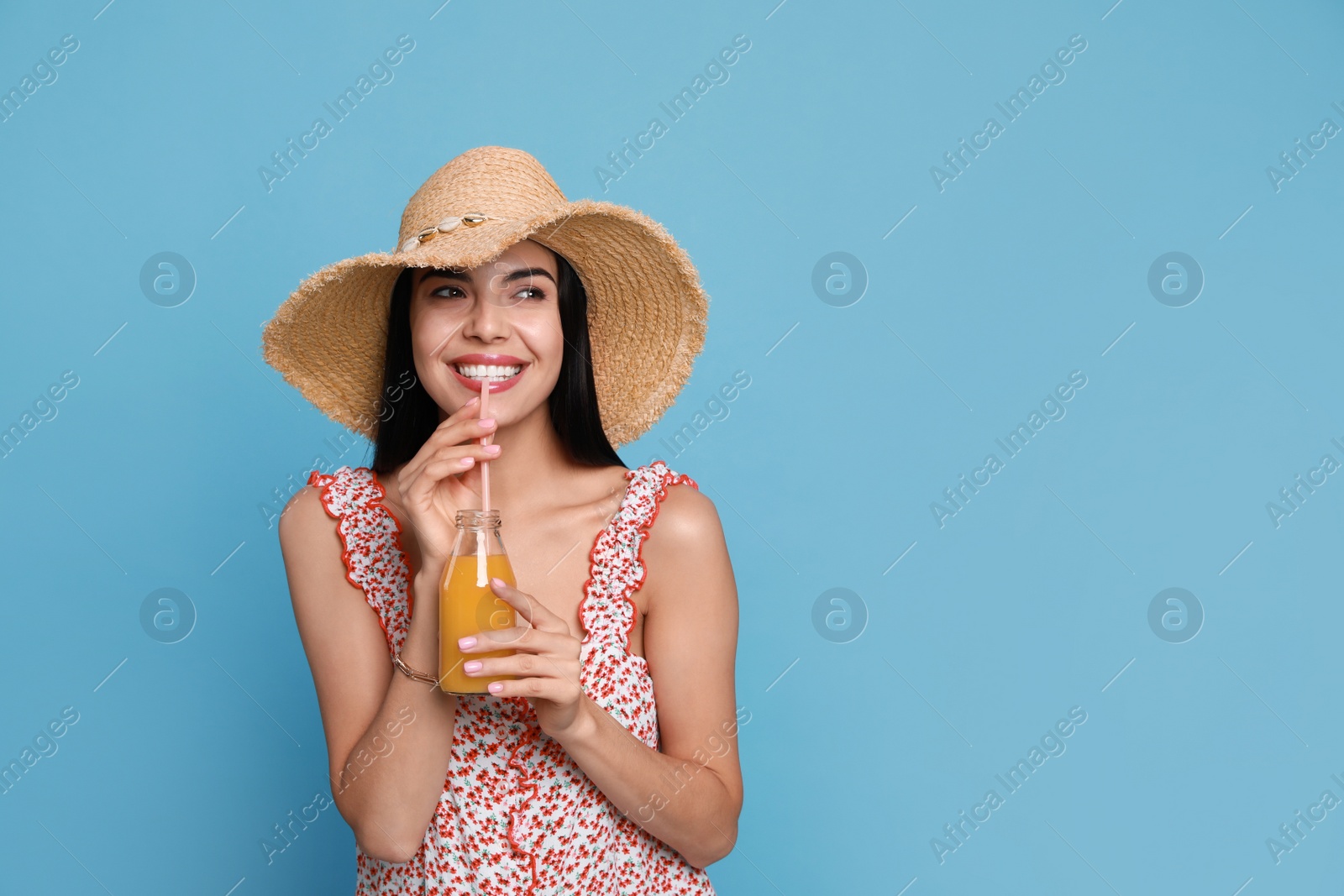 Beautiful young woman with straw hat and bottle of refreshing drink on light blue background. Space for text Photo of Beautiful young woman with straw hat and bottle of refreshing drink on light blue background. Space for text