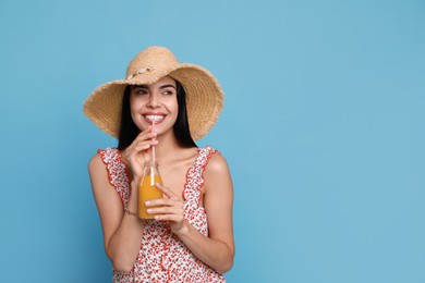 Beautiful young woman with straw hat and bottle of refreshing drink on light blue background. Space for text Photo of Beautiful young woman with straw hat and bottle of refreshing drink on light blue background. Space for text