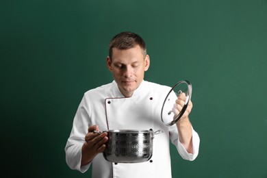 Happy male chef with cooking pot on dark green background Photo of Happy male chef with cooking pot on dark green background