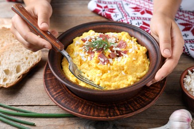 Woman eating banosh with brynza and pork cracklings at wooden table, closeup. Traditional Ukrainian dish Photo of Woman eating banosh with brynza and pork cracklings at wooden table, closeup. Traditional Ukrainian dish