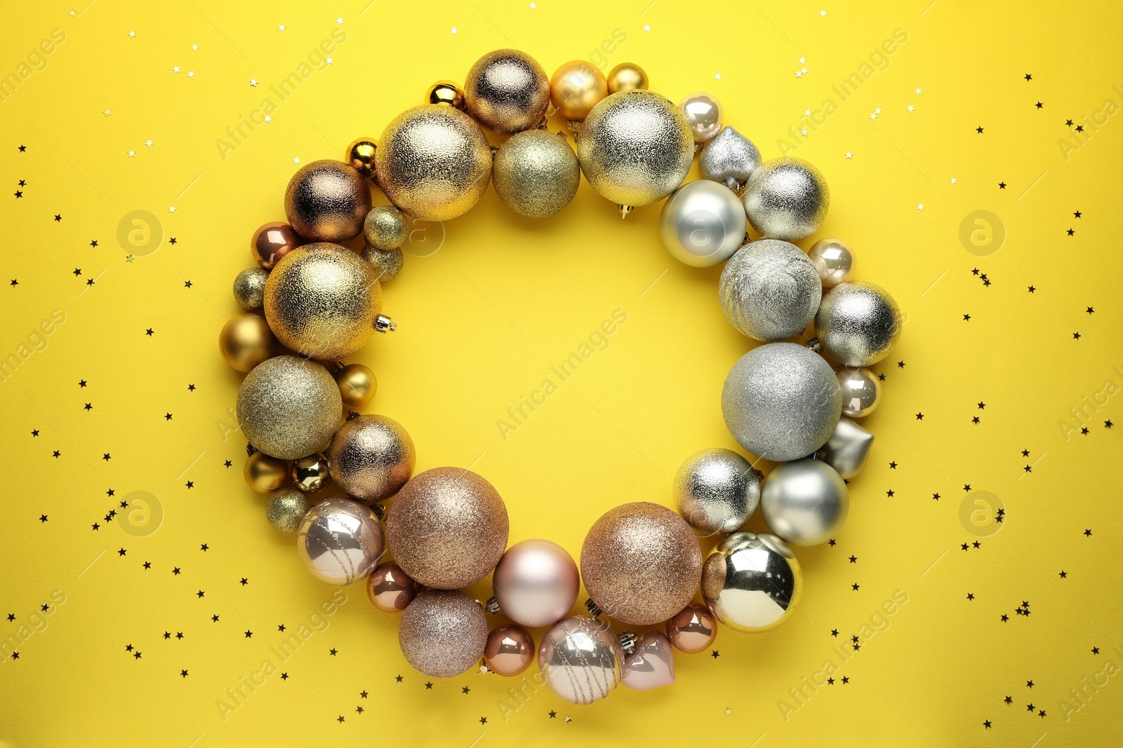 Bright festive wreath made of Christmas balls on yellow background, top view. Space for text Photo of Bright festive wreath made of Christmas balls on yellow background, top view. Space for text